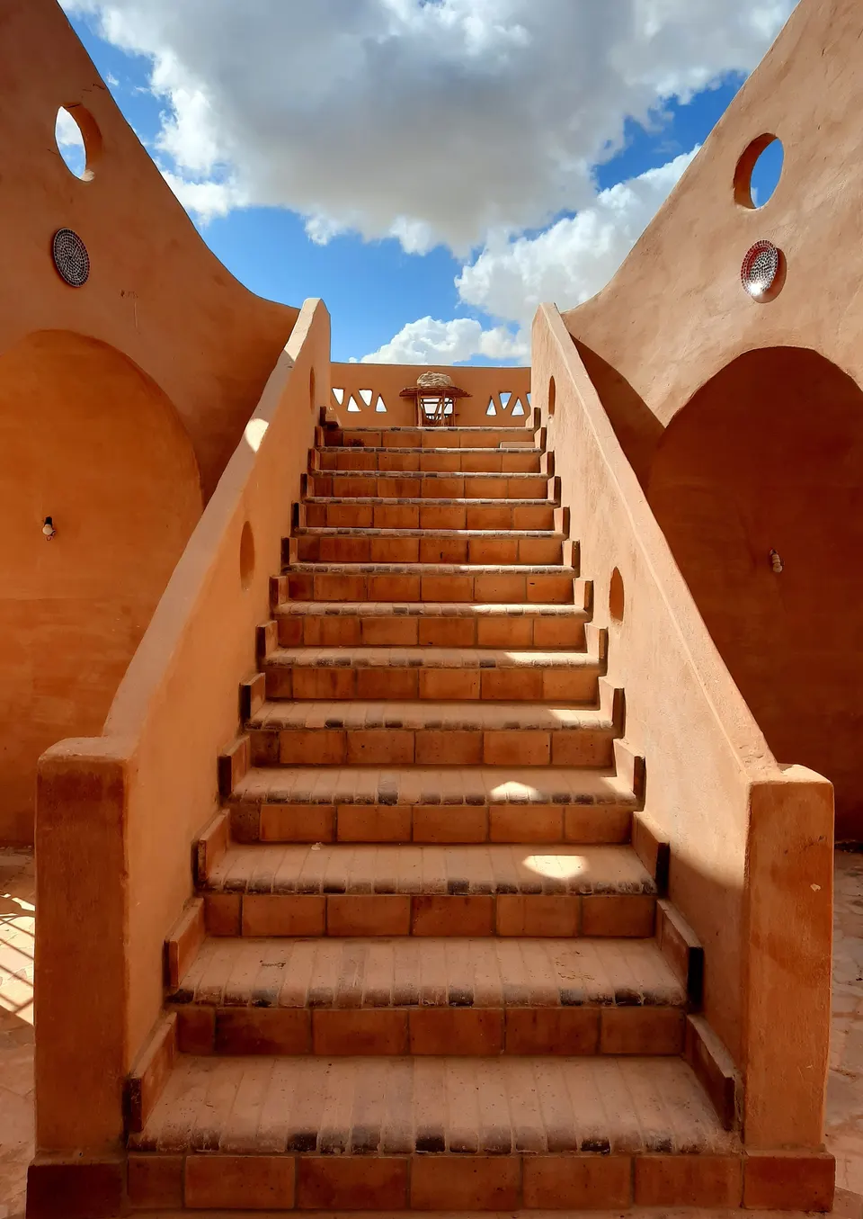 A staircase between sand-coloured walls beneath a blue sky