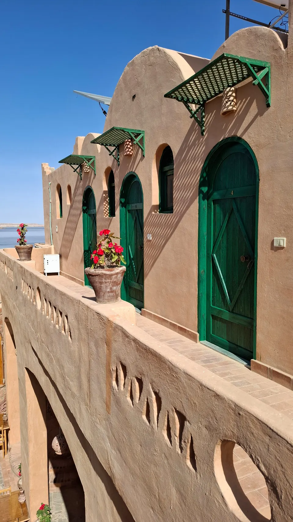Green arched doors, shaded lanterns and flowers along an upper terrace at the lodge