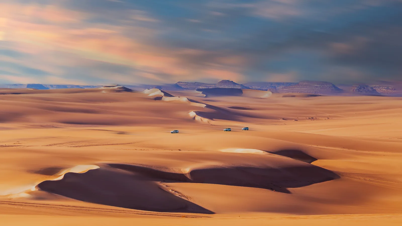 Four-wheel-drive safari vehicles among the golden dunes near Siwa.