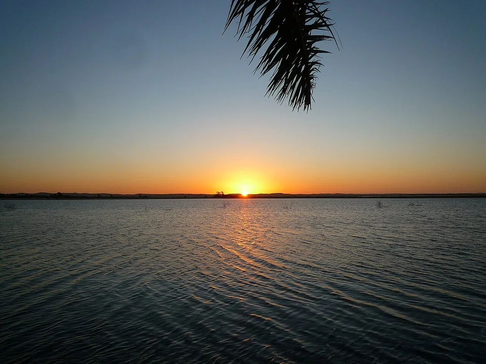 Sunset over the lake at Fatnas Island, framed by a palm frond.