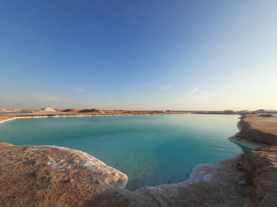 Turquoise salt pool edged by pale salt and rock near Aghurmi in Siwa.