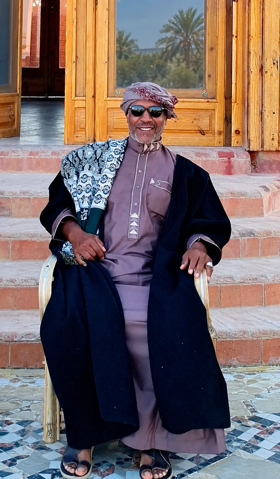 The lodge owner seated outside the wooden entrance doors